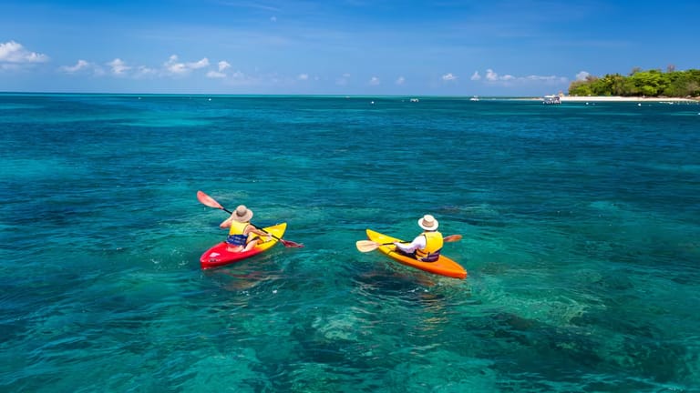 Aerial view of two red and yellow kayaks from behind. Green Island is visible in the background.
