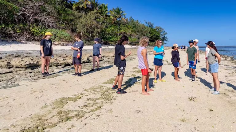 Group of school children standing around on the Green Island beach.